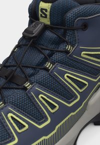 Κοντινή λήψη μπλε και πράσινου παπουτσιού πεζοπορίας με επάνω μέρος από δίχτυ, συνθετικές επενδύσεις και ρυθμιζόμενο ελαστικό σύστημα κορδονιών.