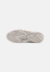 Semelle de sneaker Fila blanche présentant une surface texturée avec un motif en zigzag, des grips circulaires et un logo gravé. Design plat et large.