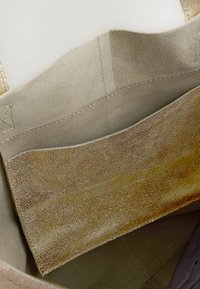 Inredningen av en mockaväska som visar beige tyg med en mjuk textur och ett ljusare, glittrande guldaccentpanel och sömnadsdetaljer.
