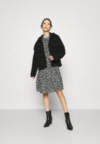 Casaco de fleece preto com dois bolsos no peito sobre um vestido floral preto, combinado com botins de salto pretos. Outfit simples e em camadas.