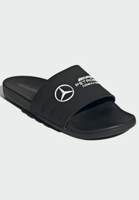 Crne natikače sa teksturiranim remenom, s bijelim Mercedes-Benz logom i natpisom "Petronas Formula One". Gumeni potplat.