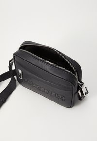 Borsa a tracolla in pelle nera con superficie testurizzata, accessori in argento, chiusura con zip e dettaglio del logo impresso sulla parte anteriore.