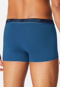 Blauwe boxershorts met een gestructureerd geometrisch patroon, elastische tailleband met "uncover" branding, en een aansluitend ontwerp.