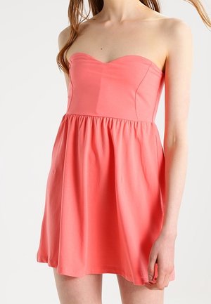 Coral strapless dress with a sweetheart neckline, fitted bodice, and a flared skirt, made of smooth fabric, featuring a gathered waist.