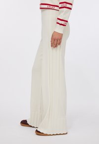 Pantaloni in maglia a costine color crema con orlo svasato, caratterizzati da righe verticali e finitura testurizzata, abbinati a scarpe scure slip-on.