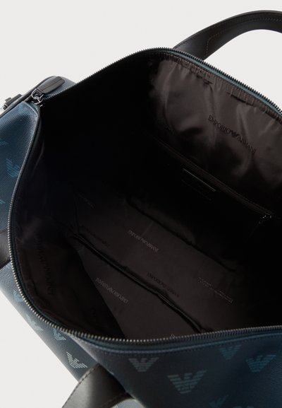 Ανοικτή μπλε τσάντα Emporio Armani που δείχνει το ευρύχωρο εσωτερικό με μαύρο ύφασμα, φερμουάρ και επαναλαμβανόμενο λογότυπο.