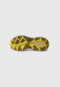 La semelle de la chaussure présente une surface brune texturée avec des accents jaunes et des rainures pour une meilleure traction. Logo imprimé sur la semelle.