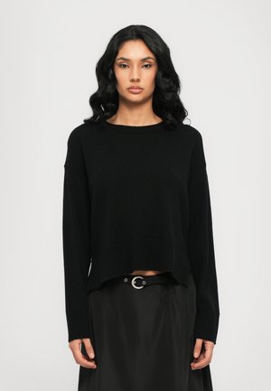 Sort strikket sweater med rund hals, dropped skuldre og ribbet kant. Båret over en sort nederdel med en sølv spænde-bælte accent.