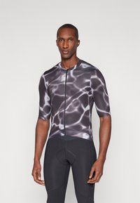 Maillot de cyclisme à manches courtes noir avec un motif abstrait évoquant l'eau, doté d'une fermeture éclair à l'avant et d'une coupe ajustée, associé à un short de cyclisme noir.