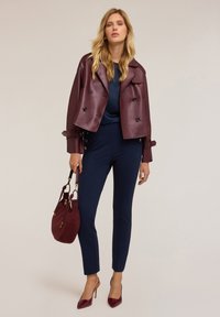 Bordeaux leren cropped jas met een dubbelzijdig ontwerp, blauwe top, marineblauwe fitted broek, kastanjebruine handtas en pumps met spitse neuzen.