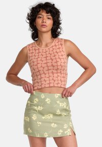 Crop top in light pink with a grid pattern, paired with a short green skirt featuring a floral print and side slit. Both are fitted.