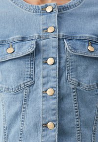 Light blue denim jacket with gold buttons down front and on two chest pockets, worn by a person.