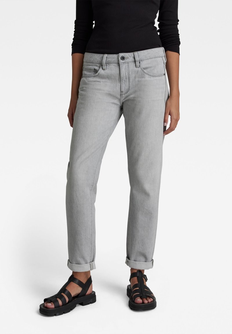 Calças de ganga cinzentas com um corte largo, cinco bolsos e bainhas dobradas. Usadas com sandálias pretas de tiras, exibindo um estilo casual.