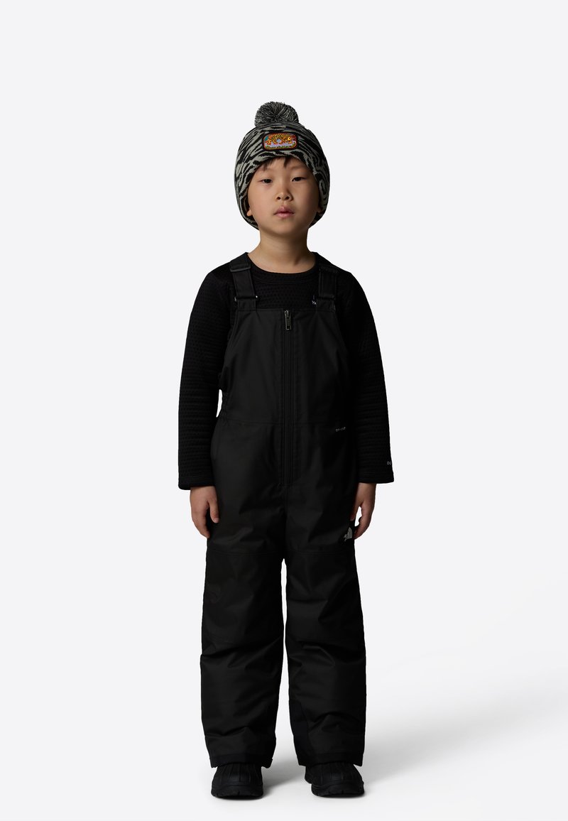 Black insulated overall with a zip front, worn over a textured black long-sleeve shirt. The child wears a patterned knit hat with pom-pom.