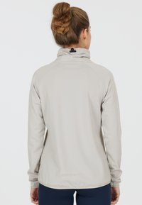 Lysegrå jakke med høj krave, raglanærmer og tekstureret stof. Har en sort spænde ved halsen og et minimalistisk design.