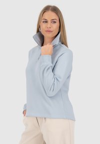 Pullover in pile azzurro chiaro con zip, colletto alto, polsini a coste e texture morbida. Presenta una zip a metà lunghezza per una facile vestibilità.