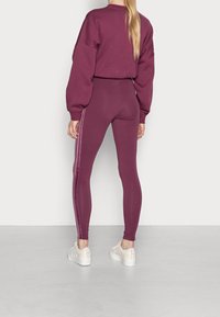 Vínová mikina a legíny s přiléhavým střihem, které mají kontrastní boční pruhy. Bílé tenisky doplňují celý outfit.