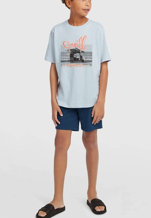 Helehall sinine puuvillane T-särk graafilise trükiga, kombineeritud tumesiniste lühikeste pükstega ja mustade slaidsetega. Reguleeritav sobivus, vabaaja disain.