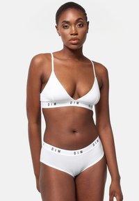 Bralette blanca con tirantes finos y un corte en V frontal; braguitas blancas a juego con una cinturilla de marca negra. Textura de algodón suave.