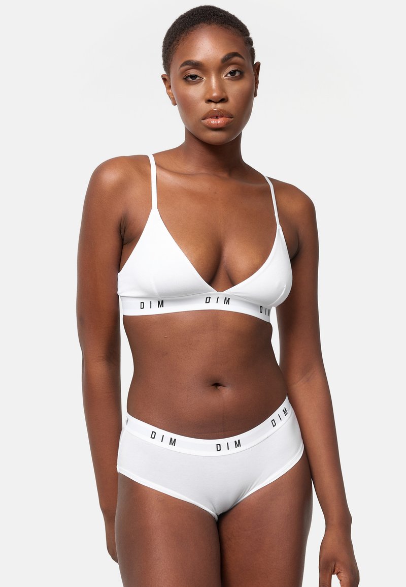 Bralette blanca con tirantes finos y un corte en V frontal; braguitas blancas a juego con una cinturilla de marca negra. Textura de algodón suave.