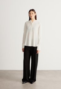 Fehér, gombos nyakú, hosszú ujjú blúz laza fekete nadrággal, sima textúrával és egyszerű kialakítással.