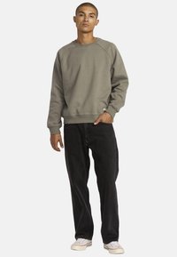 Grijze sweatshirt met ronde hals en geribbelde manchetten, gecombineerd met zwarte jeans en witte schoenen. Eenvoudig ontwerp met een relaxte pasvorm.