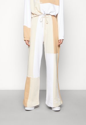 Joggings amples en coloris crème, blanc et beige, fabriqués en coton doux. Dotés d'une taille élastique et de poches latérales.