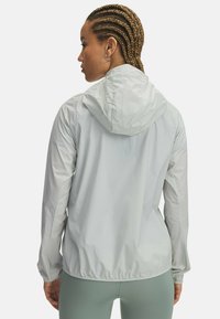 Lichtgrijze hoodie-jack gemaakt van lichtgewicht materiaal, met elastische manchetten en een getailleerde taille voor een strakke pasvorm.
