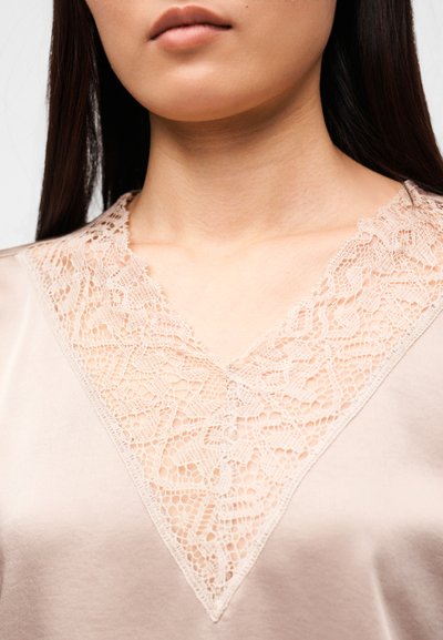 Μπλούζα από μετάξι με V-λαιμόκοψη και περίτεχνη δαντέλα σε μπεζ απόχρωση, απαλή υφή και ουδέτερο, μαλακό χρώμα.