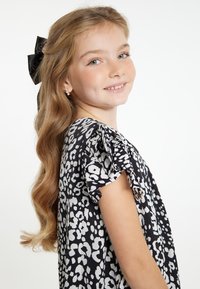 Abito bianco e nero con un design a stampa leopardo, maniche corte a volant e una texture morbida. Accompagnato da capelli lunghi e mossi e un fiocco nero.