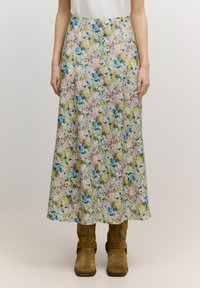 Blumiger langer Rock in einem Pastellfarbenspektrum mit blauen, rosa und gelben Blumen, aus leichtem Stoff, kombiniert mit braunen Stiefeln.