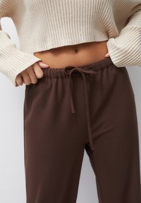 Bruine, losse broek met een koord in de taille, gecombineerd met een crème-kleurige, geribbelde, cropped trui. Zachte stoftextuur, casual ontwerp.