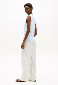 Chemise polo sans manches bleu clair avec un col, associée à un pantalon large à rayures verticales grises et blanches, vue de dos.