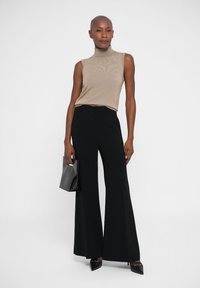 Beige ribbattu top ilman hihoja, yhdistettynä korkeavyötäröisiin mustiin leveälahkeisiin housuihin. Malli pitää mustaa clutch-laukkua ja käyttää teräväkärkisiä mustia korkokenkiä.