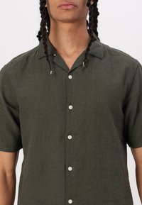 Dark green short-sleeve button-up shirt made of lightweight linen with a relaxed fit, featuring a flat collar and white buttons.