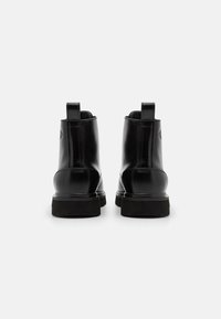 Botas de tobillo de cuero negro con un acabado liso, tacón bajo, tiradores y suelas de goma contrastantes que presentan un detalle de logo sutil.
