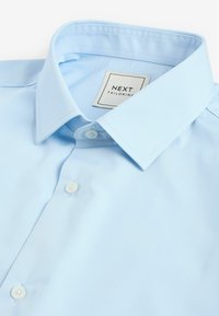 Hellblaues maßgeschneidertes Hemd aus Baumwollmix, mit langem spitzen Kragen, weißen Knöpfen und einem bedruckten Etikett mit der Aufschrift "NEXT TAILORING."