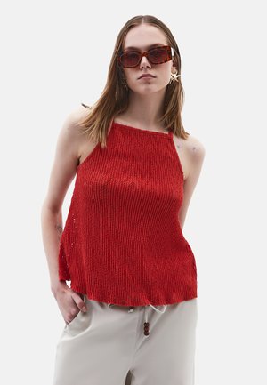 Rød strikket tanktop med et tekstureret design, brede stropper og en løs pasform. Matchet med lysebeige bukser og oversized solbriller.