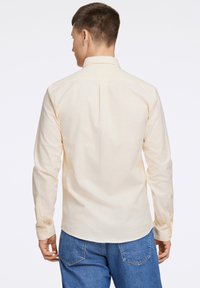 Camicia a maniche lunghe gialla chiara con colletto classico, piega sul retro e polsini con bottoni, abbinata a jeans in denim blu.