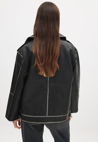 Veste en cuir noir au fit ample, avec des coutures contrastantes, un grand col et des manches longues. Texture lisse et design minimaliste.