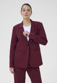 Burgundský blazer s vykrojeným klopem, zapínáním na jeden knoflík a dvěma předními kapsami. Vyrobený z hladkého materiálu s mírně strukturovaným střihem.