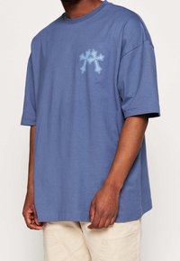 Hellblaue Baumwoll-T-Shirt mit kurzen Ärmeln und lockerem Schnitt, ausgestattet mit einem hellblauen grafischen Design auf der linken Brust und einem Rundhalsausschnitt.