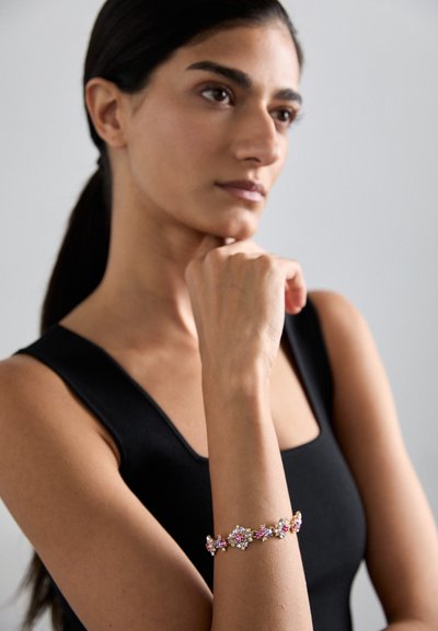 Armband in Goldoptik mit rosa und klaren Kristallen, florales Design mit markanten Akzenten, getragen am Handgelenk eines Models.