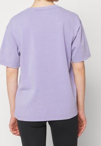 T-shirt en coton violet à coupe décontractée et manches courtes. Comprend un col rond, un détail surpiqué et une texture lisse.