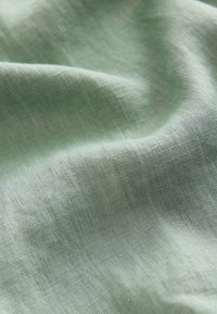 Light green linen fabric with a soft, textured surface, showing gentle folds and natural fiber weave details.