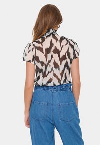Sheer blouse with a ruffled collar, featuring a brown and cream pattern; paired with high-waisted blue denim pants.