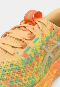 Buty sportowe Asics z oddychającą, siateczkową cholewką w odcieniach pomarańczowego, żółtego i zielonego. Szczegóły obejmują kontrastujące sznurowadła oraz teksturowaną podeszwę.