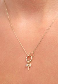 Gouden ketting met een dunne ketting, voorzien van twee in elkaar grijpende ringen en drie bedels: een hart, een sleutel en een klein kristallen hangertje.