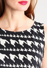 Czarna i biała sukienka w wzór houndstooth, z okrągłym dekoltem i gładką teksturą materiału. Brak widocznych zapięć lub ozdób.