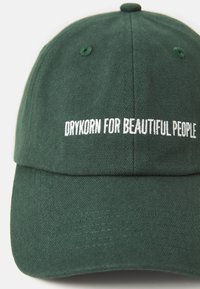 Green baseball cap made of textured fabric with white embroidered text "DRYKORN FOR BEAUTIFUL PEOPLE" on the front.